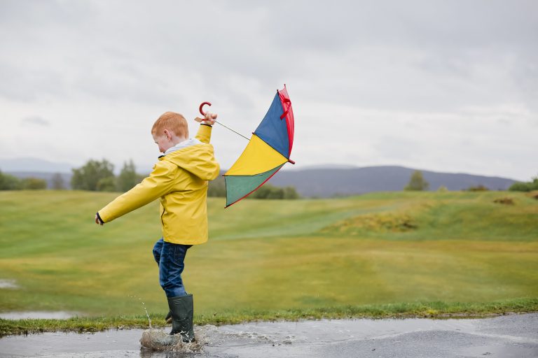 little boy with umbrella playing in the rain